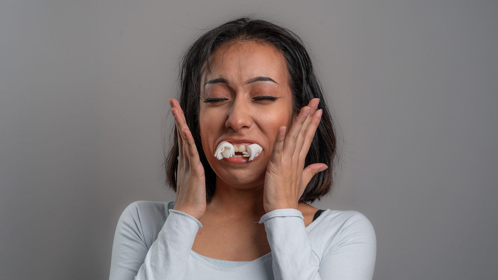 The image shows a person with their eyes closed, holding their face and making a surprised expression, possibly due to an unexpected event or sensation.